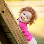 Cute little girl looking at the camera while climbing up a wooden playground.
