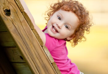 Cute little girl looking at the camera while climbing up a wooden playground.