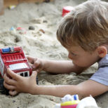 Child playing with toy car in a sandbox